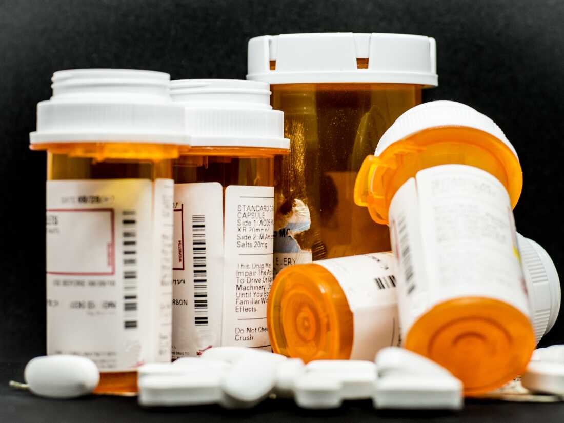 A plethora of loose prescription pills surround the bottles and US currency.